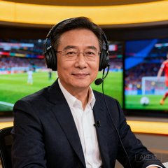 资深足球评论员周海涛的半身肖像照，他戴着耳机坐在演播室中，背景是比赛直播画面
